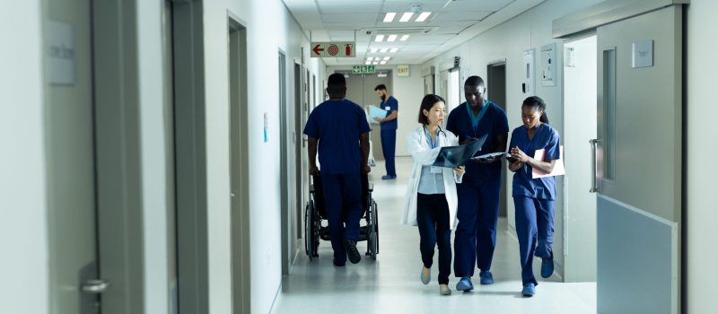 Diverse female doctor and healthcare workers discussing and walking in hospital corridor, copy space. Hospital, medical and healthcare services.